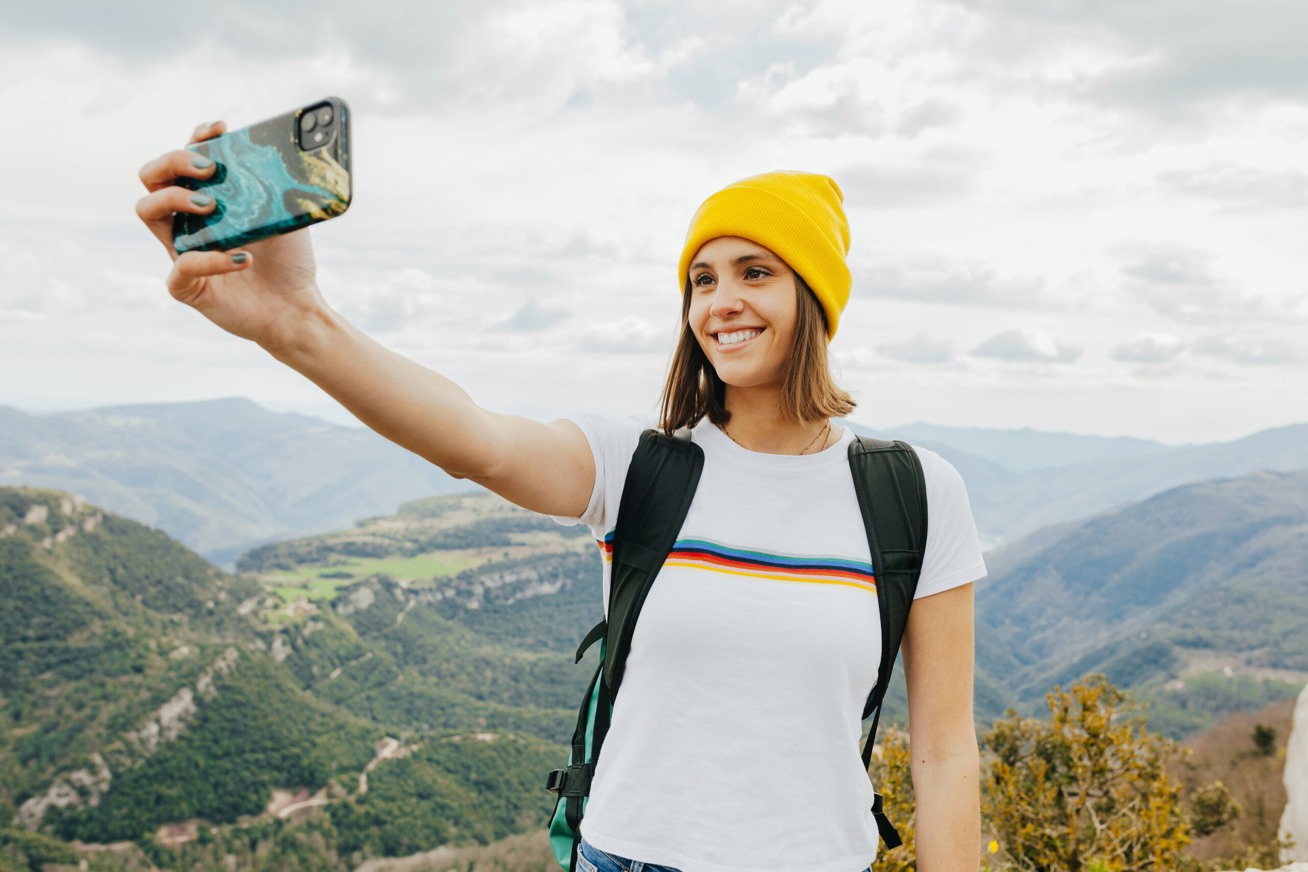 Young cheerful female backpacker taking selfie on top of mountai